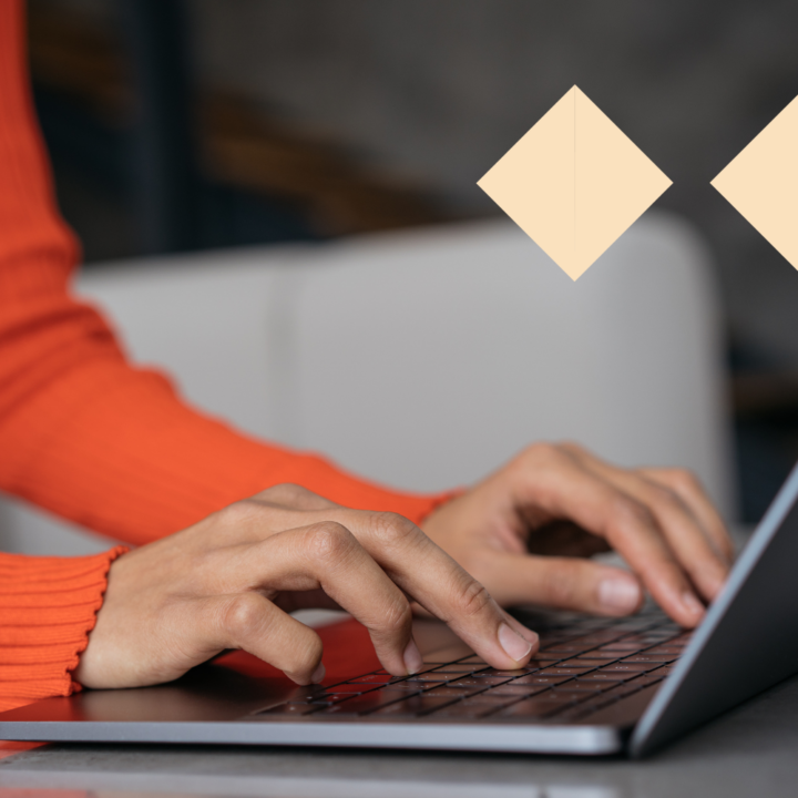 A person wearing an orange sweater typing on a laptop, working on a functional resume. The close-up shot focuses on their hands and keyboard, with a modern and minimalistic background.