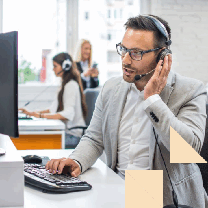 Call center employee in a gray suit sitting at a desk in front of a desktop computer talking into a headset