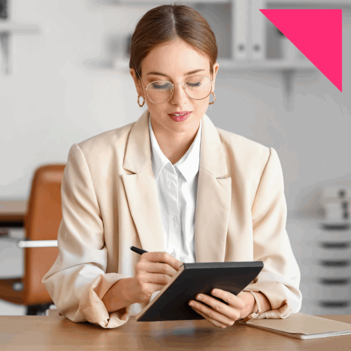 Young female professional wearing a pink suit and glasses taking notes about pay with a pen and notepad during job interview