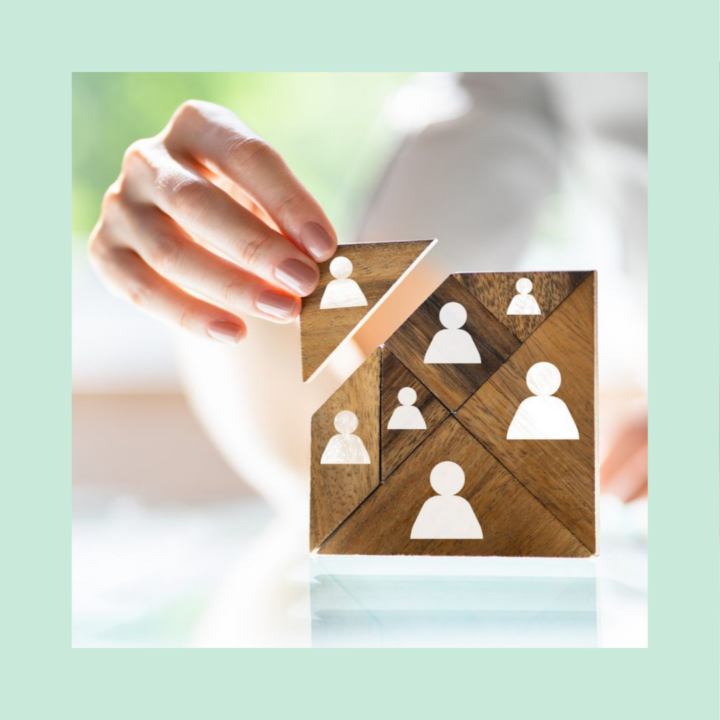 Close-up of a hand placing a triangular wooden puzzle piece into a wooden puzzle made of person icons, representing out-of-the-box recruiting ideas, creative hiring strategies, and building the right team.