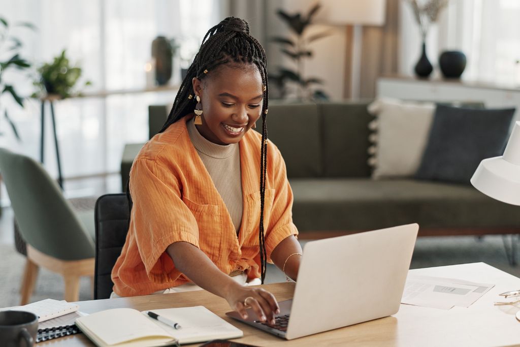 Smiling recruiter in an orange blouse at her desk typing an email with a calendar open next to her