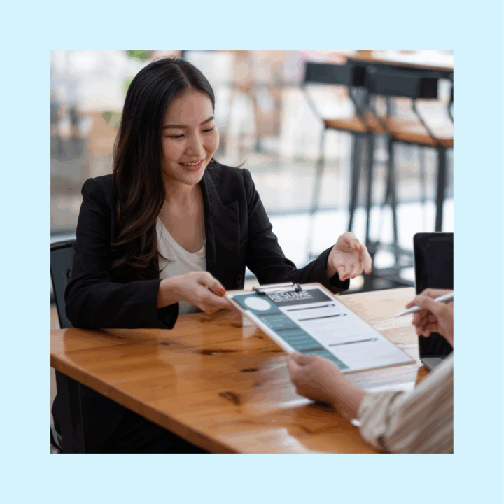 Smiling female professional in a blazer handing over a resume during a job interview