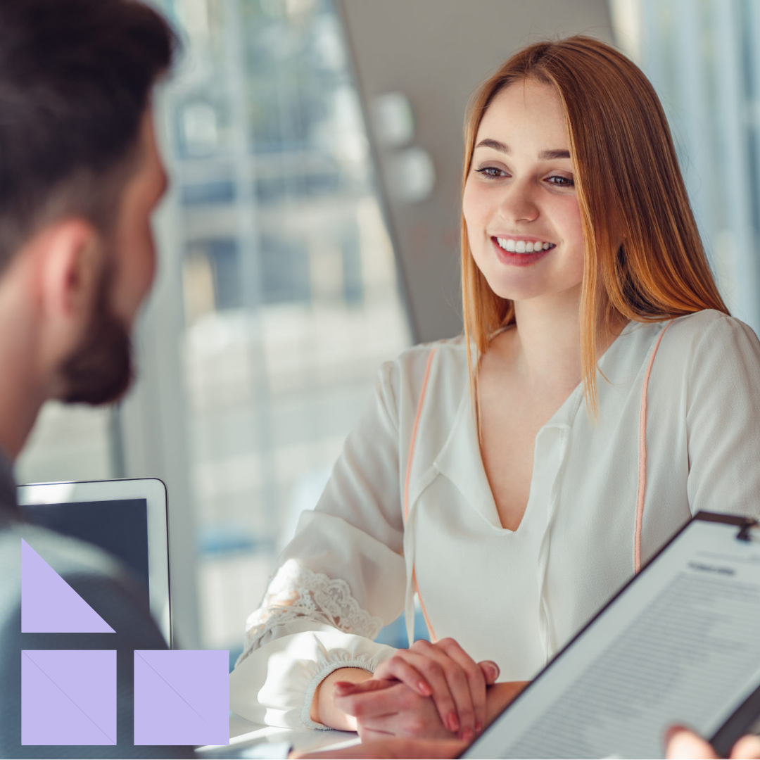 Businessman giving female job candidate interview feedback, sitting at desk in workplace on chair with a clipboard in his hands