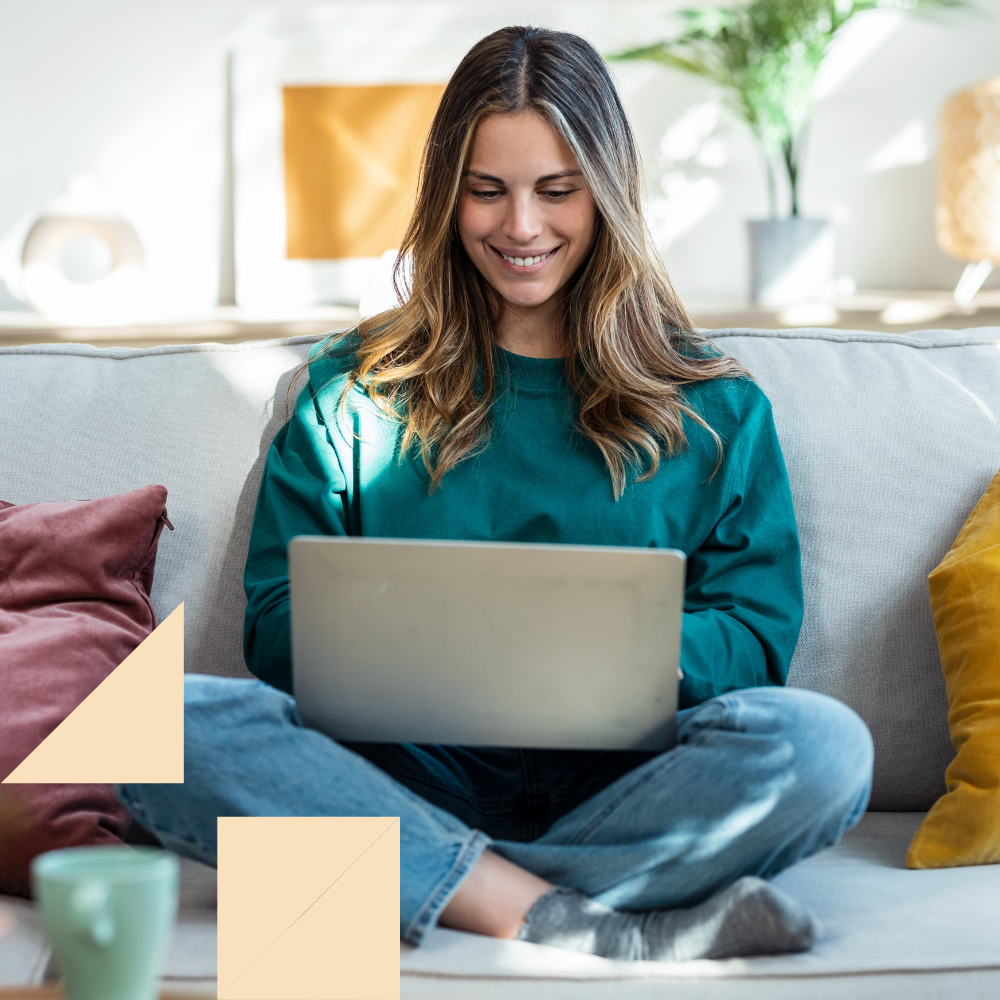 Young female job seeker sitting on her couch smiling at her laptop in her lap. Looking for a recruiter to help her get a job.