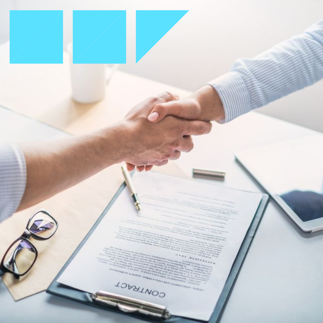 Professional shaking hands with HR professional above a contract to hire agreement that was just signed.