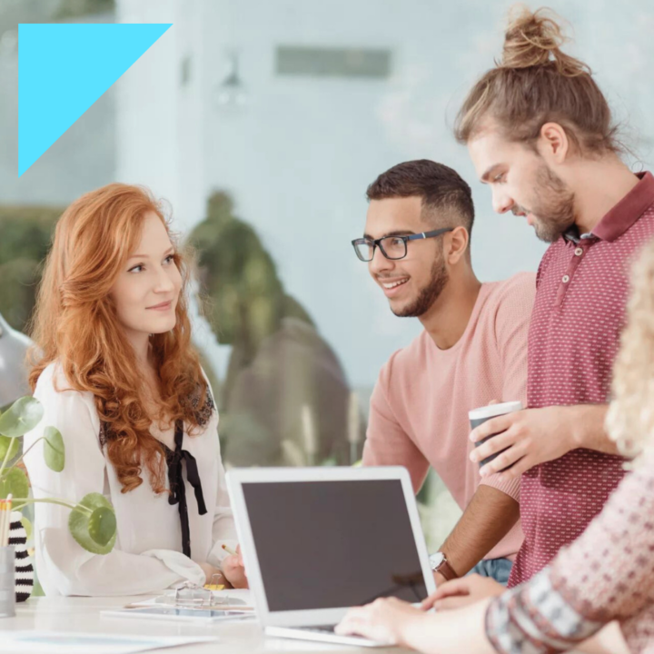 Four diverse interns working at a desk surrounding a computer smiling