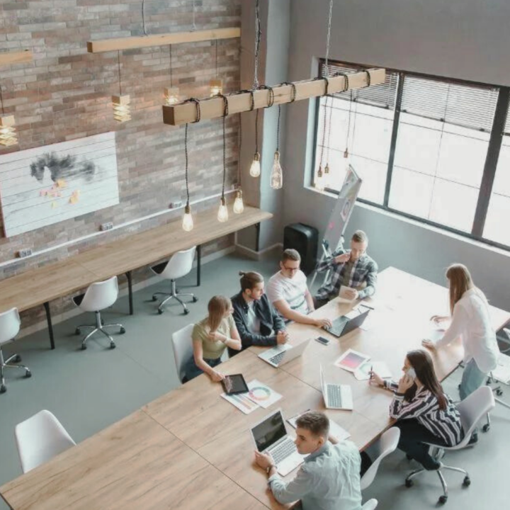 Employees gathered around large desk in a modern office with empty desks surrounding them due to a hiring freeze