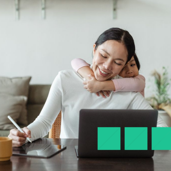 Mom sitting in front of a laptop using her apple pen to write her stay at home mom resume on her iPad with her young child wrapped around her