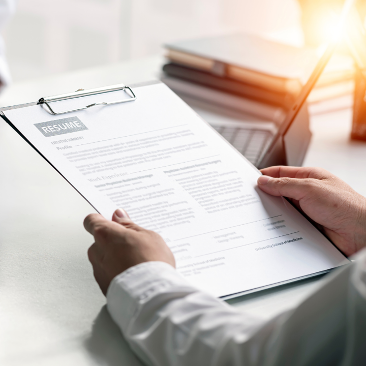A person holding a printed resume on a clipboard, reviewing its contents. The document includes sections such as "Executive Summary" and "Work Experience."