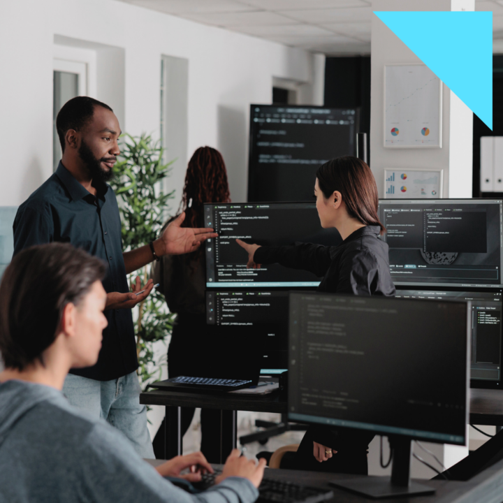 A diverse team of software developers collaborating in a modern office, discussing code displayed on multiple computer monitors. One team member gestures while another points at the screen, engaged in problem-solving