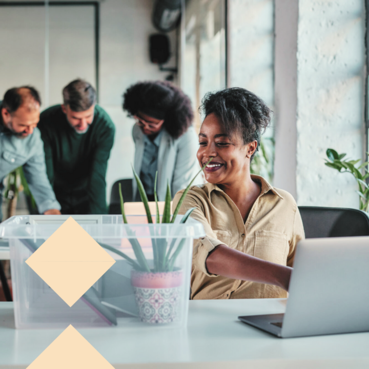 Adult businesswoman unpacking her box with belongings after she returned to work in the office while her coworkers working behind