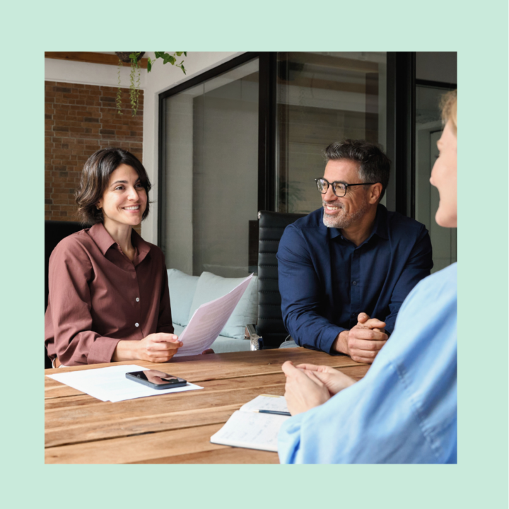 Three professionals sitting at a conference table engaged in a friendly customer service interview, with one person holding a resume and smiling.