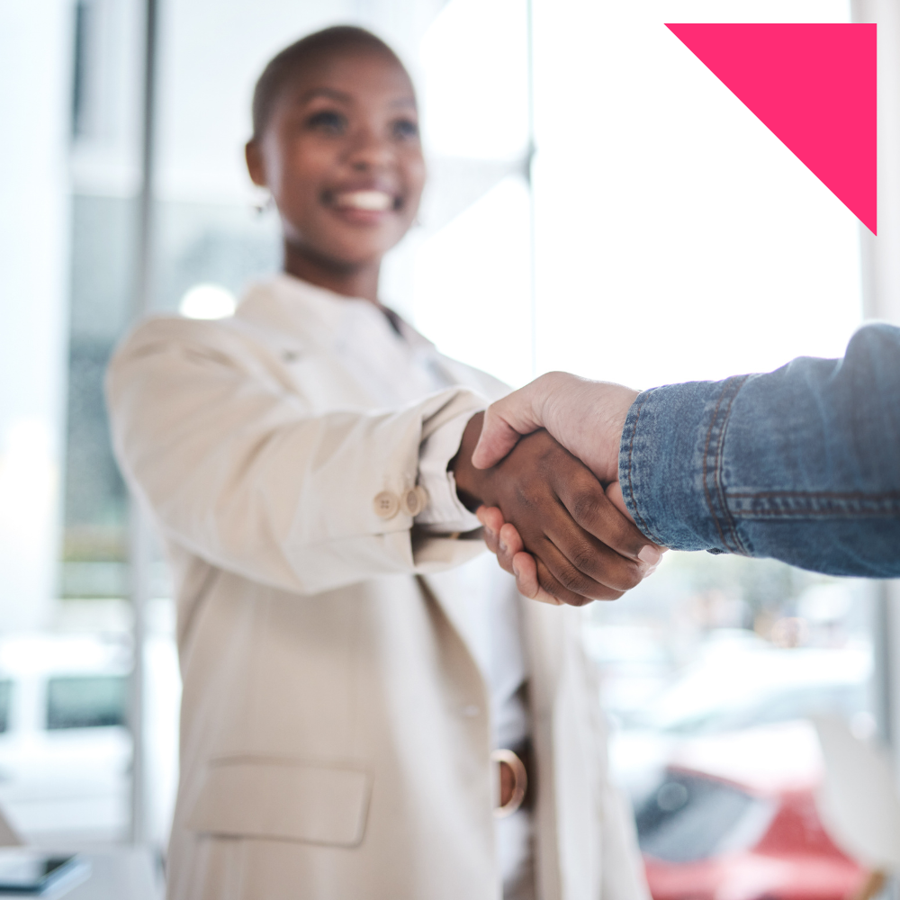A professionally dressed woman recruiter smiles as she shakes hands with another person in a bright, modern office setting, symbolizing a successful staffing partnership or agreement.