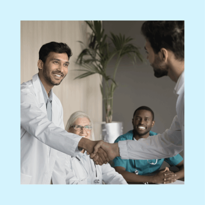 Smiling healthcare professionals in a panel setting, with a male doctor extending a handshake to a candidate, symbolizing a successful healthcare job interview or new hire.