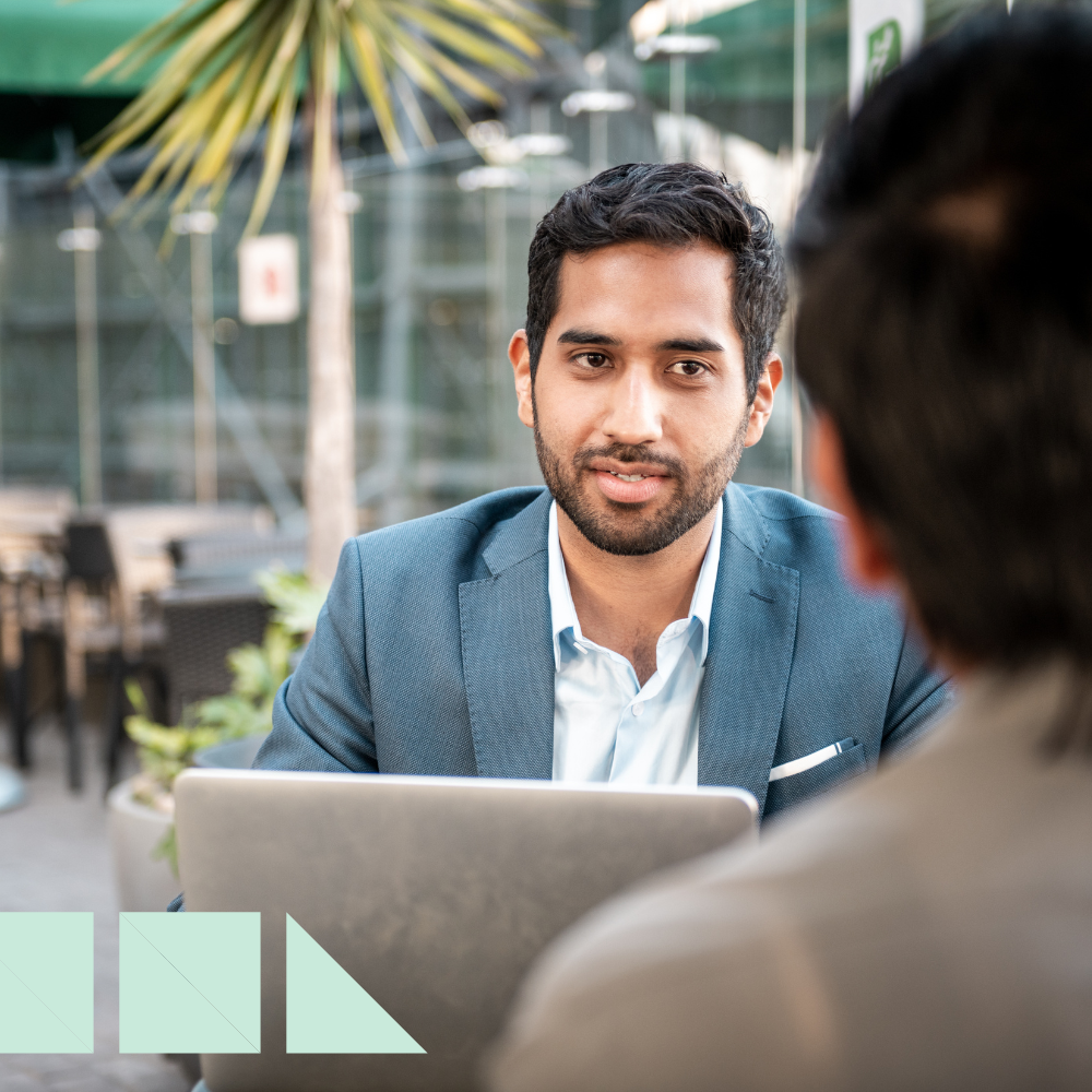Hiring manager asking admin interview questions to a candidate during an outdoor interview, with a laptop open and professional attire.