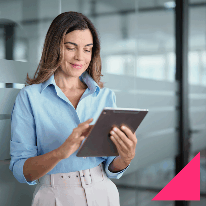 Female CMO professional in business casual smiling and typing on an iPad in an office setting