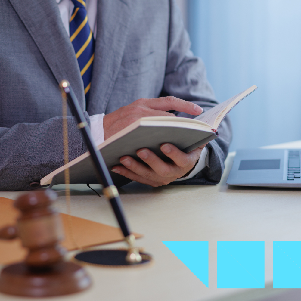Business professional in a suit reading a notebook at a desk with a gavel, pen, and laptop—symbolizing legal recruiting or law firm hiring.