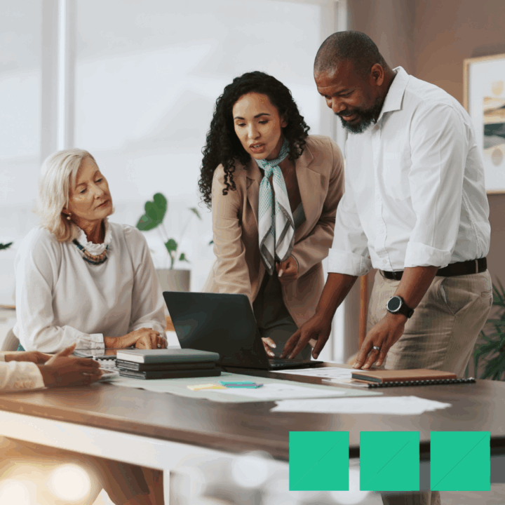 Three hiring managers gathered around a laptop in a modern office, reviewing resumes and discussing recruitment strategies to avoid the high cost of a bad hire.