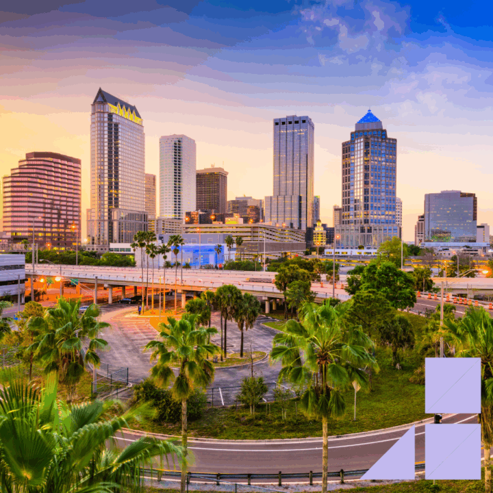Downtown Tampa, Florida skyline at sunset with modern high-rise buildings, palm trees, and highways in the foreground.
