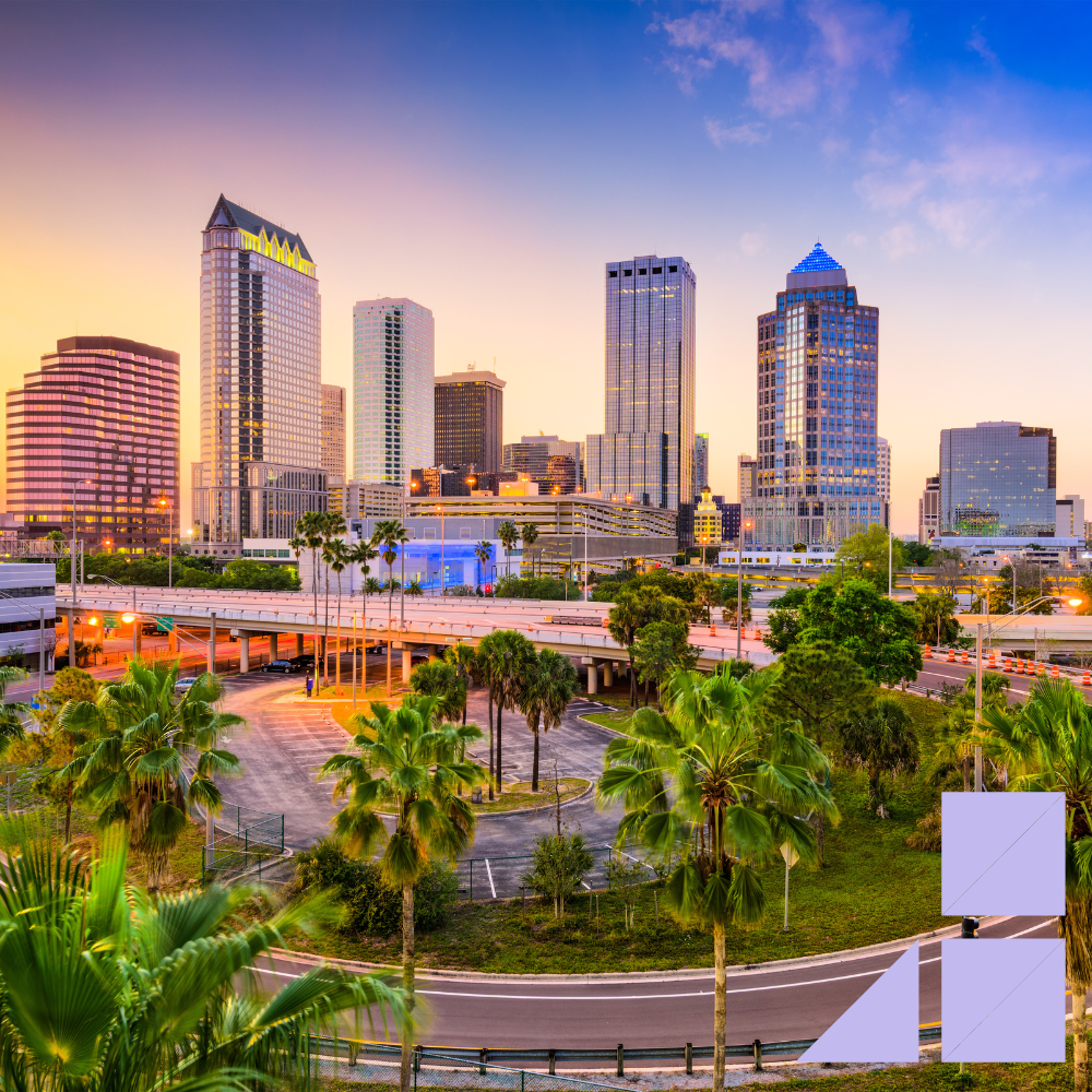 Downtown Tampa, Florida skyline at sunset with modern high-rise buildings, palm trees, and highways in the foreground.