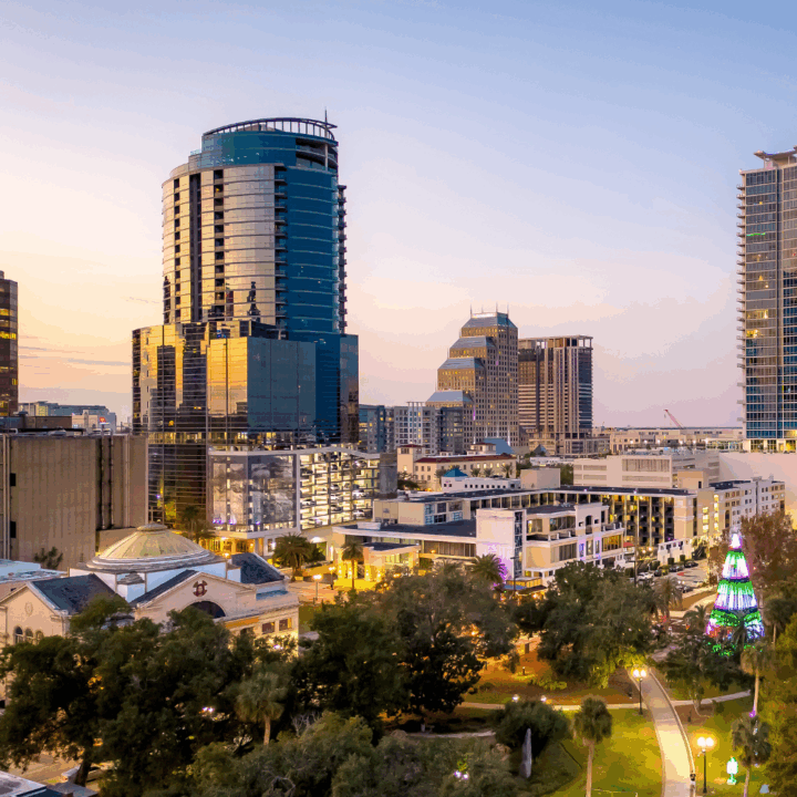 Downtown Orlando skyline at sunset featuring modern office buildings, parks, and trees in the foreground, representing the city’s vibrant business and hiring landscape.