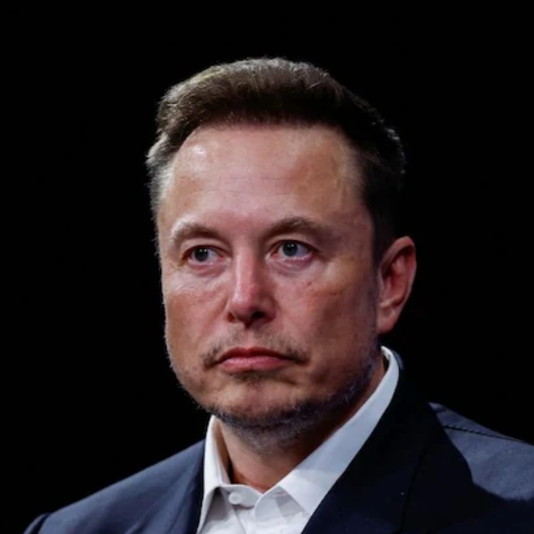 A close-up portrait of Elon Musk in a dark suit and white shirt against a black background, looking slightly off-camera with a serious expression.