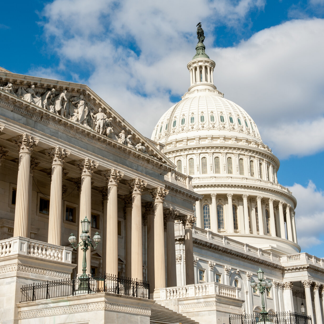 The U.S. Capitol building in Washington, D.C., with its white dome and classical columns visible under a partly cloudy blue sky.
