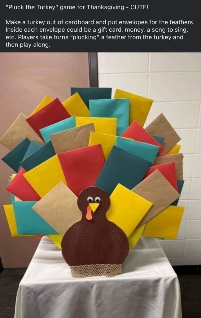 A colorful Thanksgiving turkey craft display made from paper card and envelopes, featuring a brown turkey with googly eyes and layered tail feathers created from red, yellow, teal, and tan rectangular papers arranged in a fan shape, set on a white table against a neutral wall.