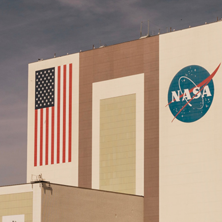 A large NASA facility with the U.S. flag painted on one side and the NASA logo on the other, set against a cloudy sky.