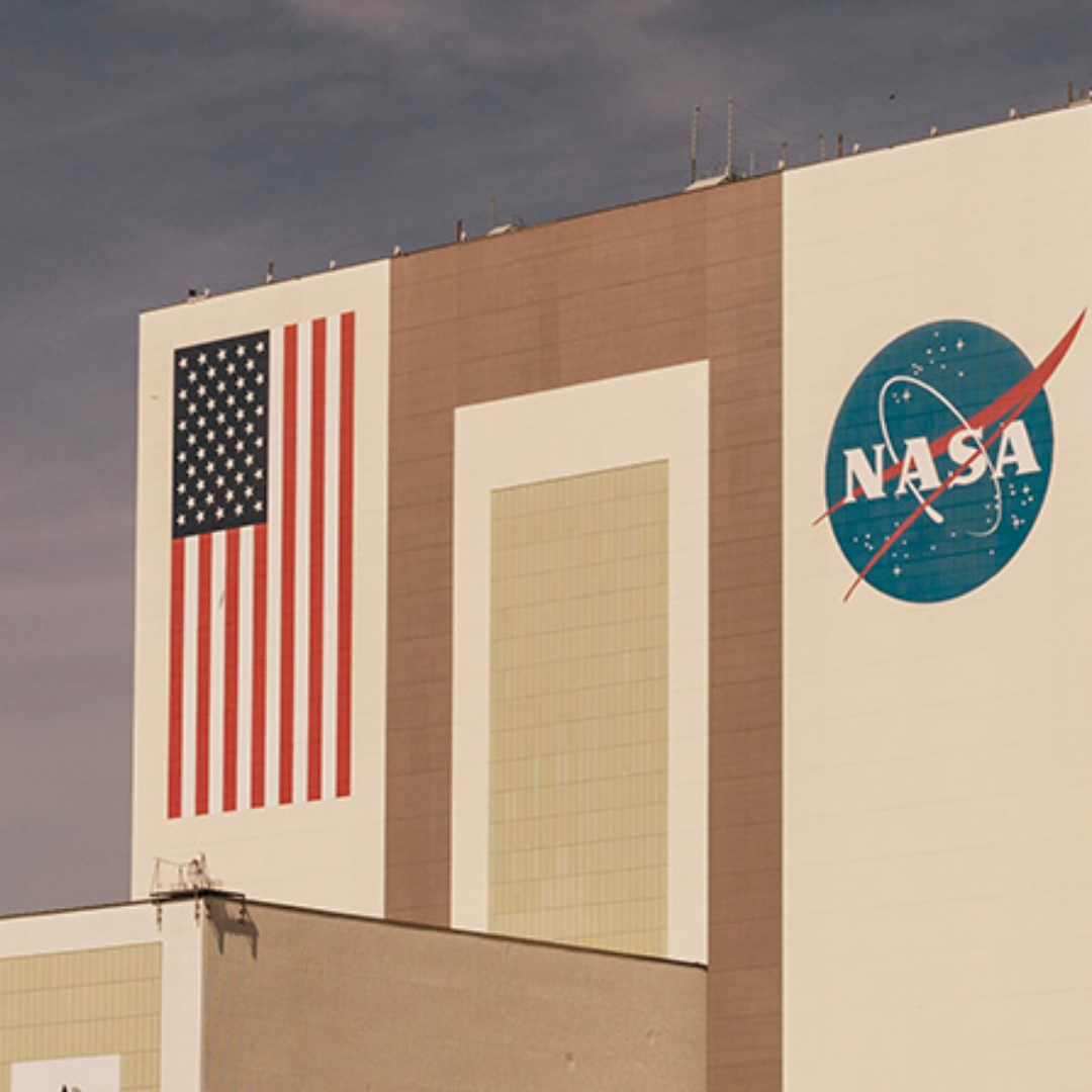 A large NASA facility with the U.S. flag painted on one side and the NASA logo on the other, set against a cloudy sky.