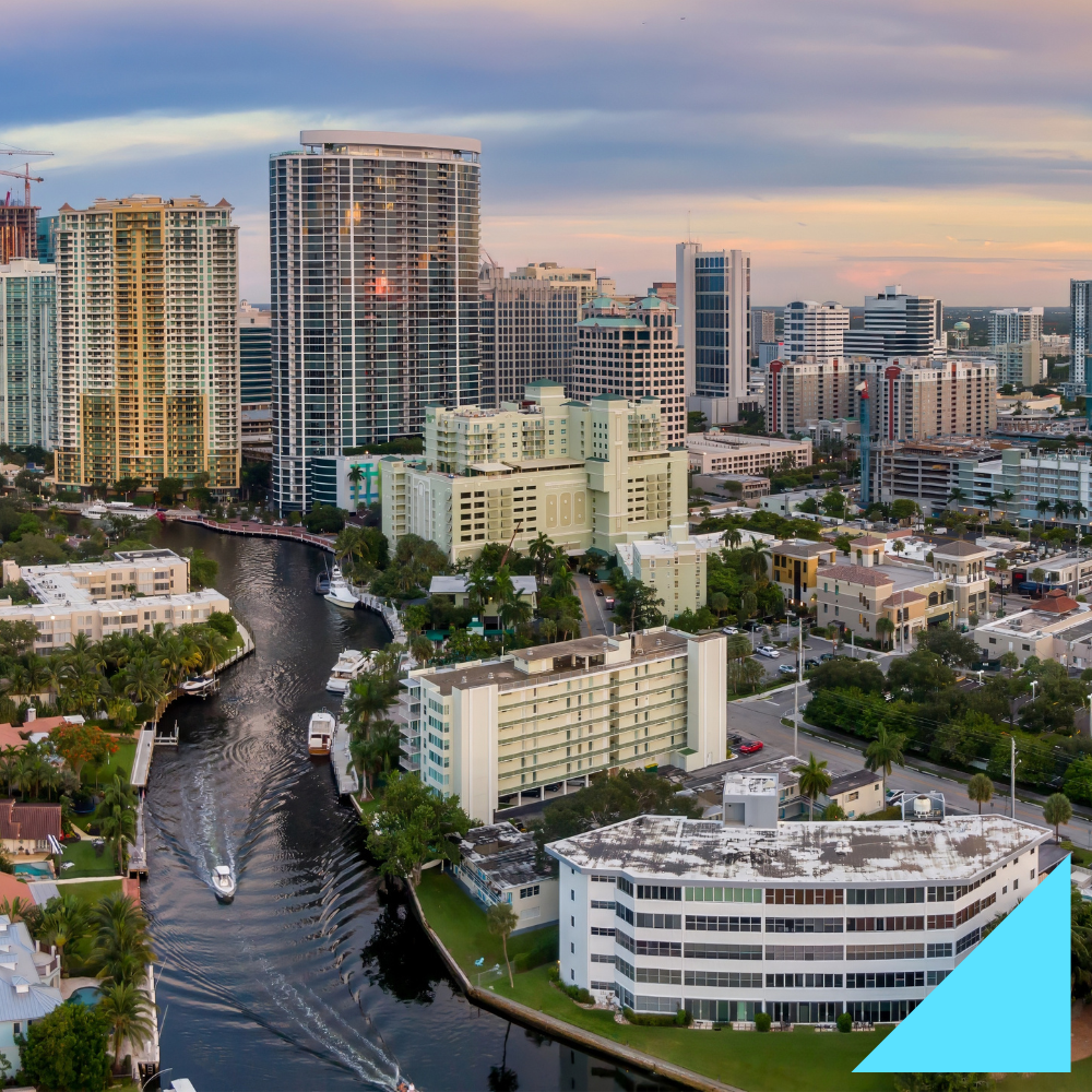 Aerial view of downtown Fort Lauderdale, Florida at sunset, showcasing high-rise buildings, palm trees, and boats navigating the canal, representing the city’s thriving business and hiring scene.