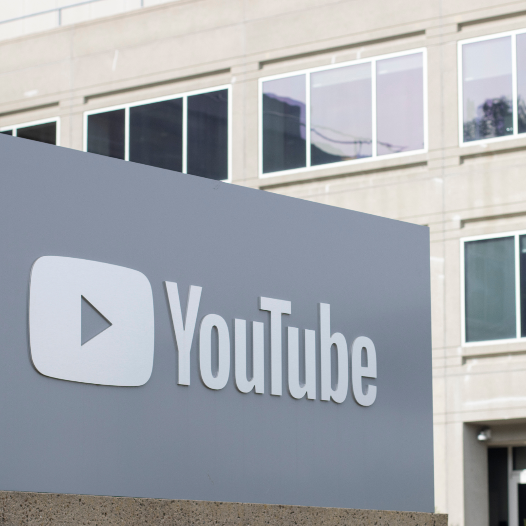 A large YouTube logo sign is displayed outside an office building, with windows and the building exterior visible in the background.