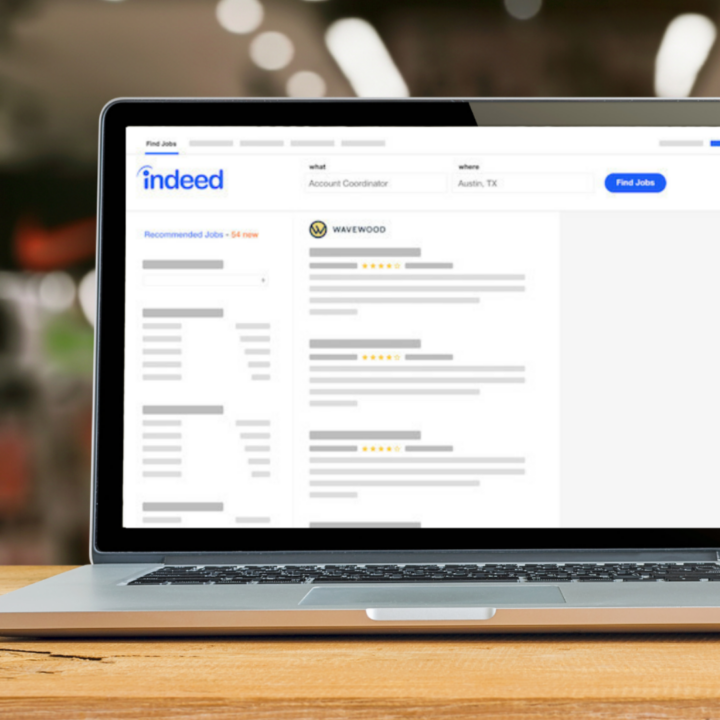 A laptop on a wooden desk displays the Indeed job search website, showing a list of job postings and search filters on the screen.