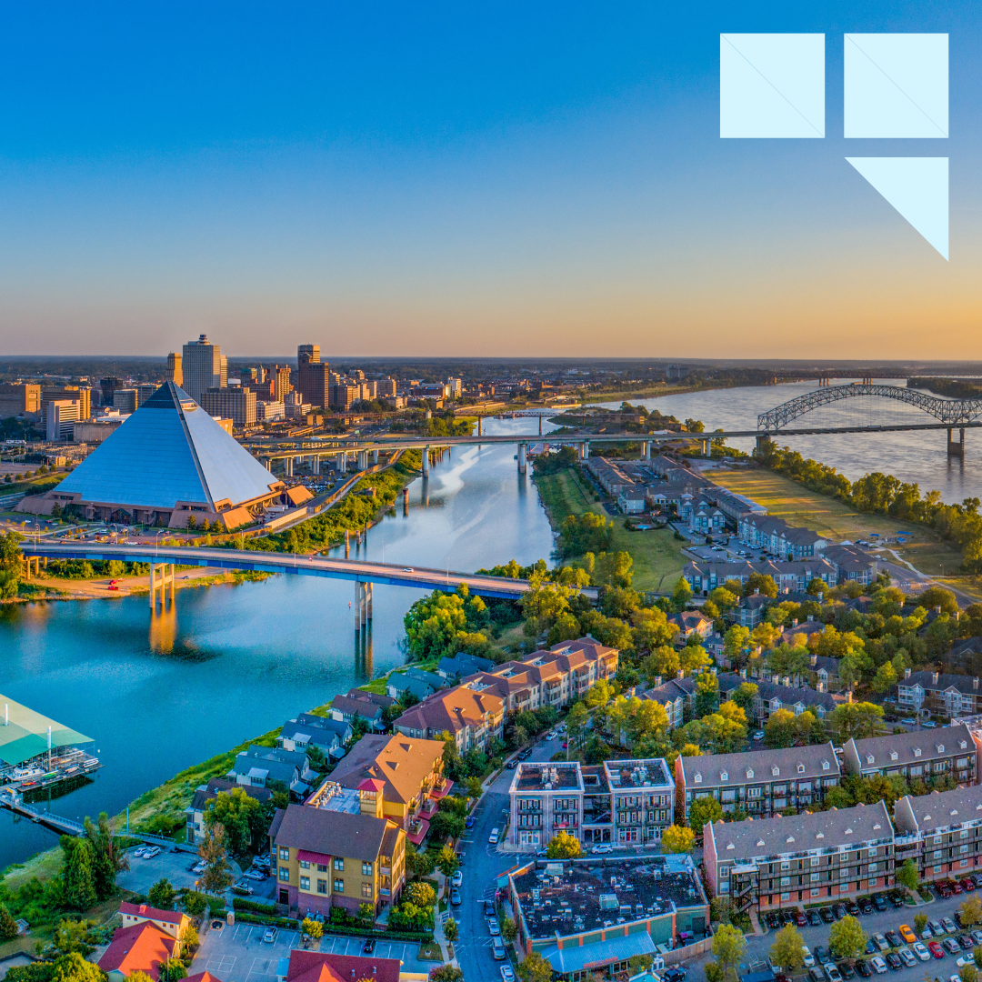Aerial view of downtown Memphis, Tennessee at sunset, featuring the Mississippi River, the Hernando de Soto Bridge, and the iconic Bass Pro Pyramid surrounded by city buildings and greenery.