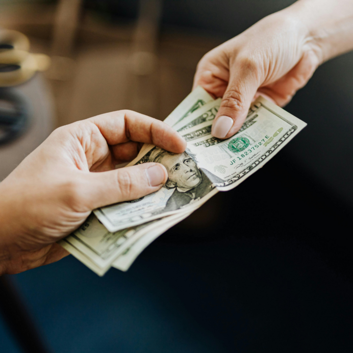 Hands exchanging U.S. dollar bills, representing worker pay, wages, compensation discussions, and income expectations.