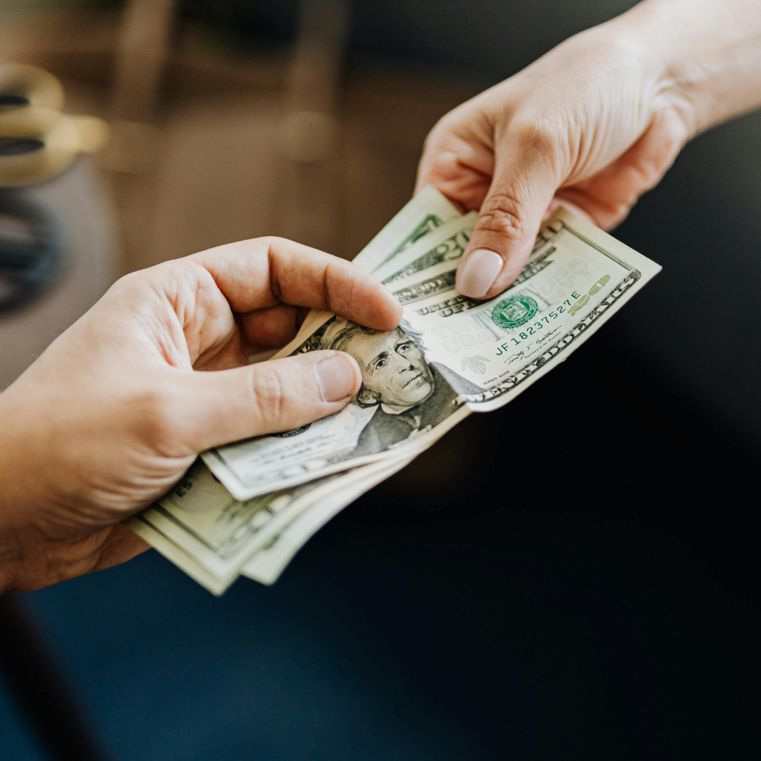 Hands exchanging U.S. dollar bills, representing worker pay, wages, compensation discussions, and income expectations.