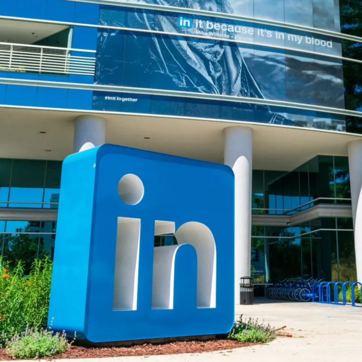 Large LinkedIn logo displayed outside a modern office building, representing the professional networking platform and corporate workplace environment.