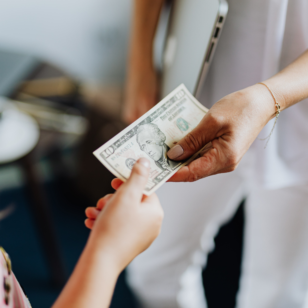 Close-up of a person handing a ten-dollar bill to another person, symbolizing payment, compensation, or a financial transaction related to work or services.