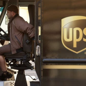 UPS delivery driver seated in a brown UPS truck, with the UPS logo visible on the vehicle’s exterior.