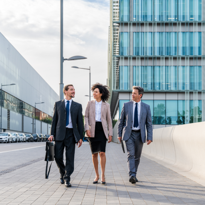 Three business professionals walking together outside modern office buildings, representing workforce trends, professional collaboration, and the evolving corporate environment.