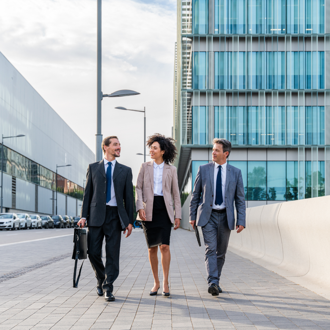 Three business professionals walking together outside modern office buildings, representing workforce trends, professional collaboration, and the evolving corporate environment.