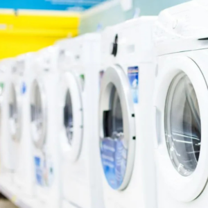 Row of white commercial washing machines in a laundromat, shown in a clean, brightly lit environment.