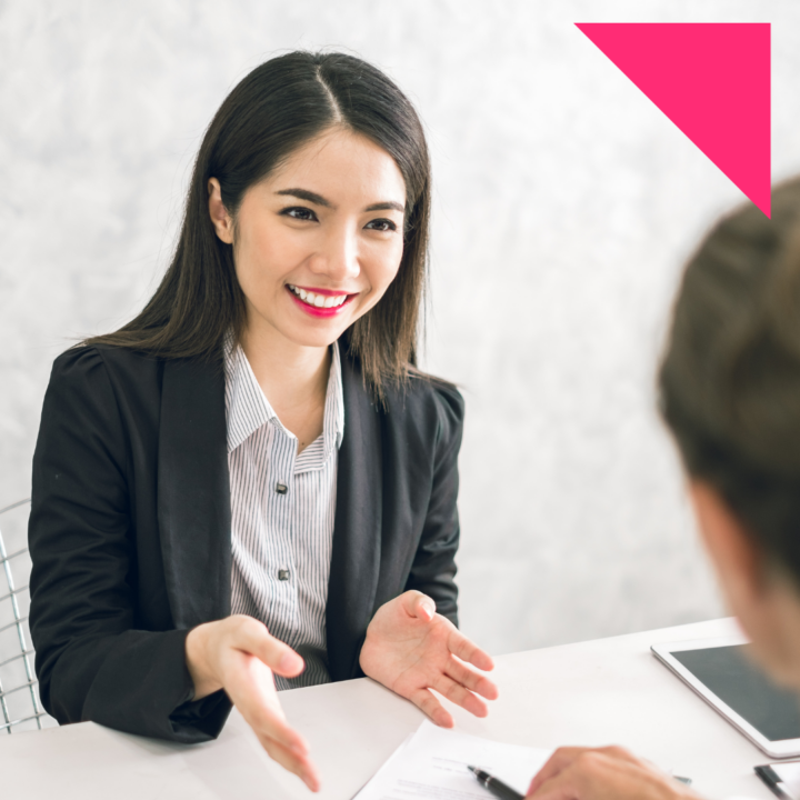 Female hiring manager smiling and gesturing while asking a fun, conversational interview question to a job candidate across a desk