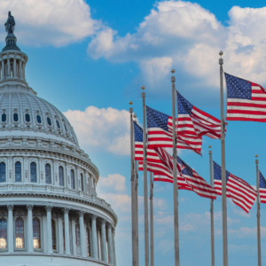 U.S. Capitol dome with multiple American flags flying in front against a blue sky with clouds, symbolizing government and national economic news.