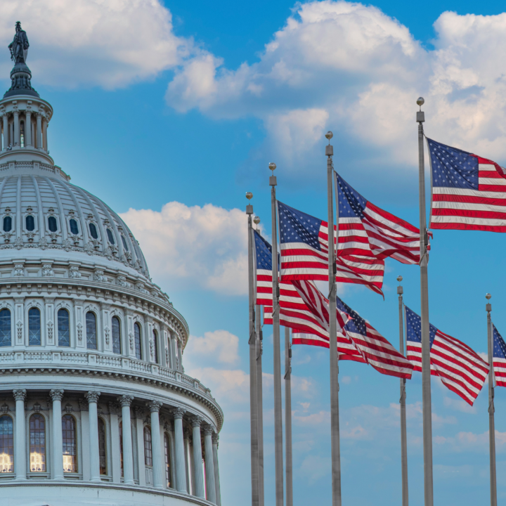 U.S. Capitol dome with multiple American flags flying in front against a blue sky with clouds, symbolizing government and national economic news.