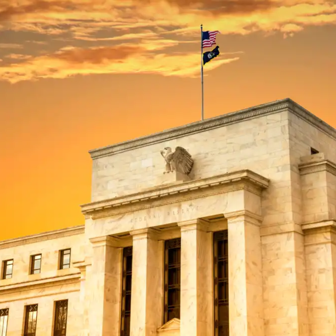Federal Reserve building with U.S. flag on top, set against a warm sunset sky.