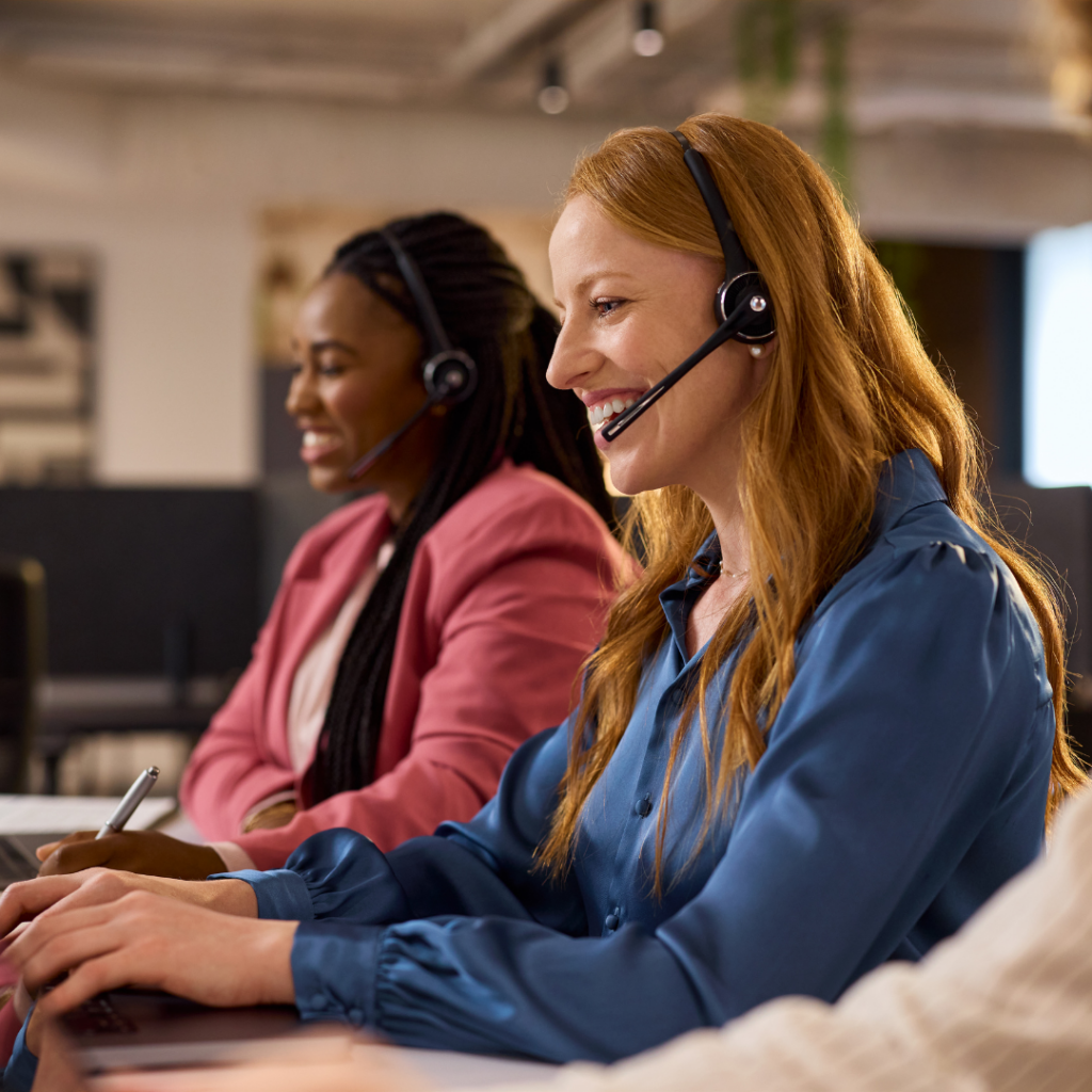 Two call center agents wearing headsets and smiling while taking calls at their desks