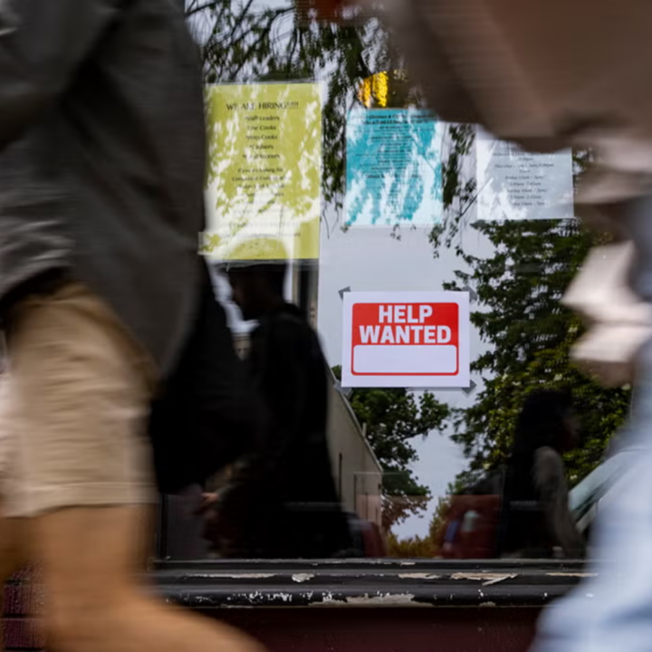 "Help Wanted" sign and hiring flyers posted in a storefront window as blurred pedestrians walk past
