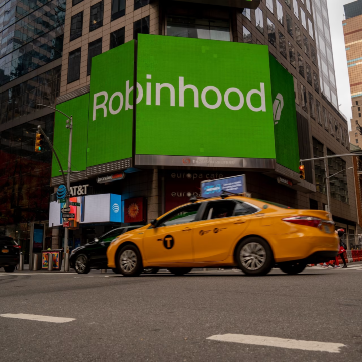 Large green Robinhood digital billboard displayed on a New York City building, with a yellow taxi passing on the street below