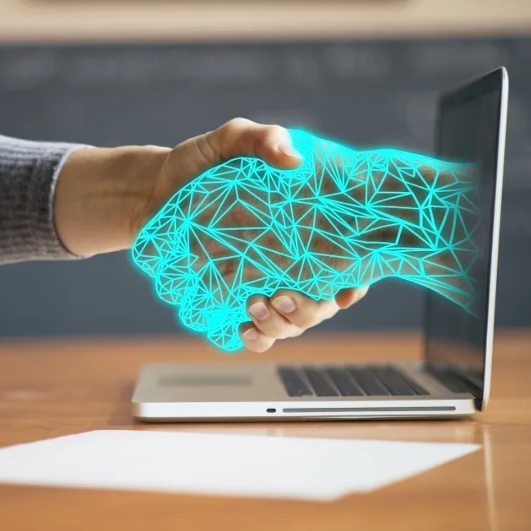 Human hand shaking a glowing digital geometric hand emerging from a laptop screen, representing virtual connection or online agreement